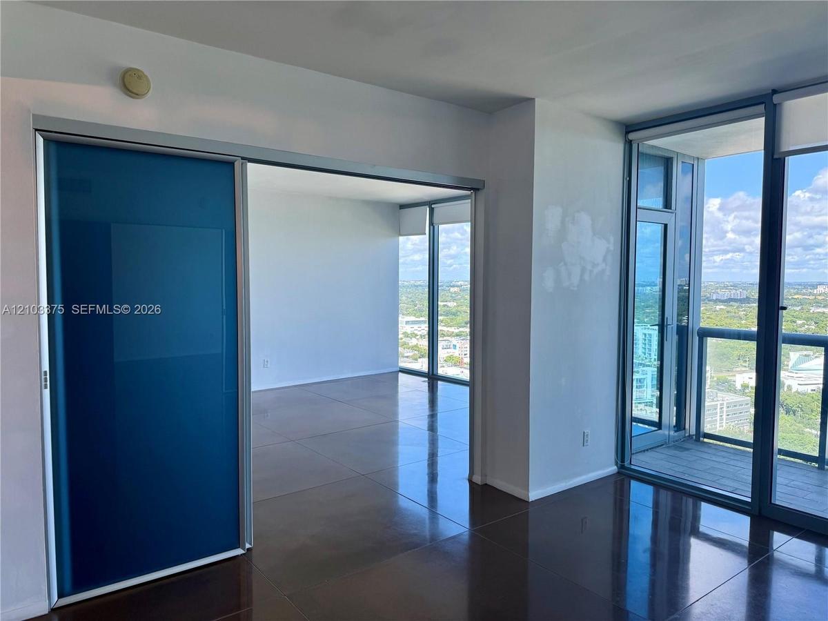 Floor-to-ceiling windows, blue-tinted sliding glass room divider, polished tile flooring, and a private balcony