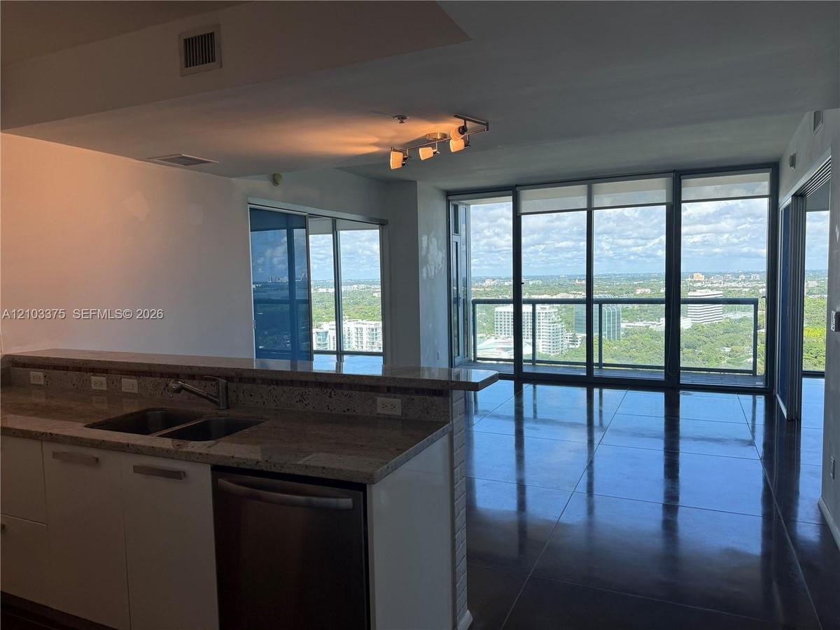 Open-concept kitchen featuring stone countertops, an integrated dual-basin sink, and a stainless steel dishwasher