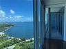 Floor-to-ceiling glass walls, expansive balcony with stone tile flooring, and metal-framed exterior door