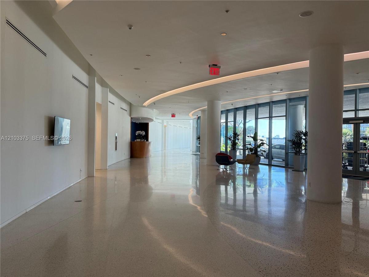 Expansive lobby featuring polished stone flooring, floor-to-ceiling glass paneling, integrated recessed ceiling lighting, and structural support colum