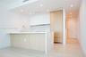 Kitchen featuring wood-finish cabinetry, white matte upper cabinets, stone-surfaced island with waterfall edge, integrated refrigerator, and recessed 