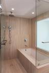 Walk-in shower and bathtub combination featuring floor-to-ceiling stone-tiled walls, glass enclosure, polished chrome rainfall shower head with handhe