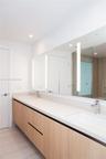 Floating wood-finish double vanity featuring integrated rectangular sinks, expansive countertop, full-width mirror with integrated lighting, and polis