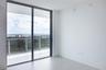 Floor-to-ceiling glass sliding doors opening to a private balcony with a glass railing and expansive horizon backdrop, featuring light-toned flooring 
