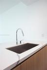 Undermount stainless steel kitchen sink with a high-arch chrome pull-down faucet, stone-finish countertop with veining, and flat-panel wood-finish cab