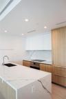 Kitchen featuring a central island with a stone countertop and waterfall edge, custom wood-finish cabinetry, white upper cabinets, integrated stainles