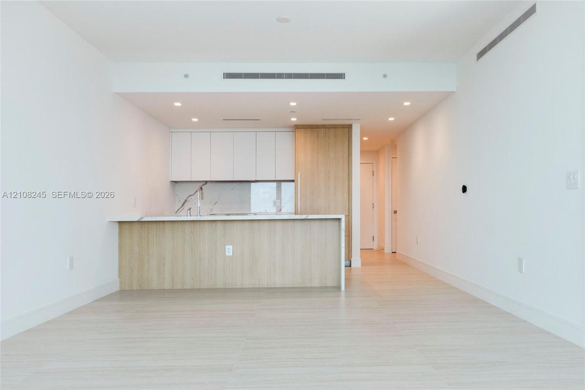 Kitchen featuring flat-panel cabinetry, light-toned wood-finish panels, stone-surface countertops, recessed ceiling lighting, and wood-finish flooring