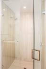 Walk-in shower enclosure featuring floor-to-ceiling neutral stone-finish tile, frameless glass paneling, polished chrome hardware, and an integrated w