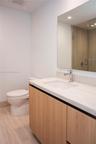 Bathroom featuring a wood-finish vanity with a light-toned countertop, integrated rectangular sink, polished chrome faucet, and a frameless wall mirro
