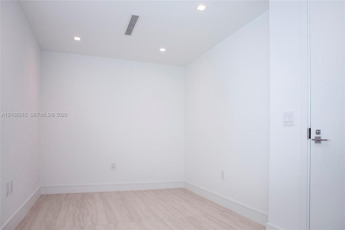 Minimalist interior featuring white wall finishes, wood-finish flooring, and recessed ceiling lighting