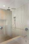 Walk-in shower featuring large-format tile surround, recessed wall niche, chrome rainfall shower head, handheld sprayer, and polished chrome hardware