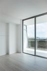 Floor-to-ceiling windows, wood-finish flooring, and a glass-paneled balcony