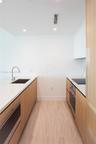 Kitchen galley featuring light wood-finish cabinetry, white stone-finish countertops, an undermount sink with a gooseneck faucet, a built-in oven, and