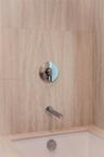 Large-format stone tile wall surround, polished chrome single-handle pressure balance valve, and integrated chrome tub spout