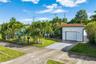 Single-story stucco exterior featuring a concrete driveway, attached garage, shingle roof, and mature palm landscaping