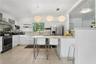 Kitchen featuring flat-panel white cabinetry, stainless steel appliances, quartz countertops, a tile backsplash, and three suspended geometric pendant