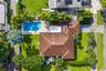 Aerial perspective featuring a shingled roof, an inground swimming pool, paved patio areas, and manicured landscaping with mature palm trees