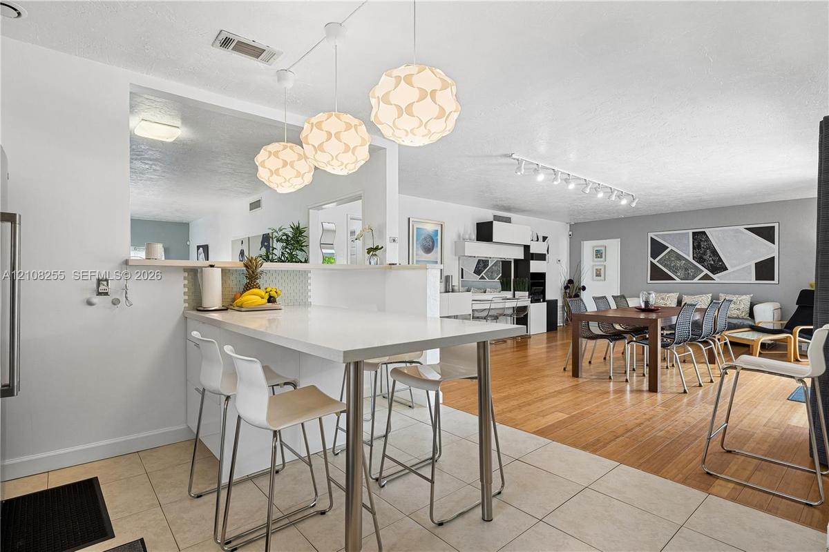 Kitchen peninsula with a solid-surface countertop and integrated breakfast bar, complemented by three spherical pendant light fixtures, large-format t