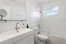 White vanity with an integrated sink, wall-mounted mirror, glass-enclosed shower and tub combination, and brushed-finish metal faucet
