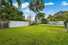 Fenced backyard featuring a manicured lawn, palm trees, an in-ground pool with a built-in slide, and privacy wall enclosure