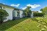 Single-story exterior featuring white stucco siding, a charcoal-trimmed bay window, mature palms, and expansive lawn