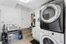 Laundry area featuring a stacked washer and dryer, white shaker-style cabinetry, an integrated basin sink, and tiled flooring