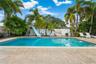 In-ground swimming pool featuring a built-in slide, surrounded by a paved deck and mature palm trees enclosed by a privacy wall