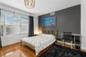 Room featuring wood-finish flooring, a charcoal accent wall, a large window with blinds, and a contemporary spherical chandelier