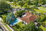 Aerial perspective of a property featuring an in-ground swimming pool, a patio area with a pergola, roof-mounted solar panels, and mature palm landsca