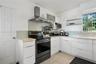 Kitchen featuring white flat-panel cabinetry, light-colored tile backsplash, stainless steel range with overhead ventilation hood, neutral countertops