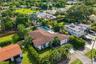 Aerial perspective of a single-story residence featuring a shingled hip roof, a private rectangular swimming pool, integrated solar panels, and manicu