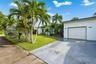 Single-story exterior featuring white stucco siding, a paved driveway, a one-car garage, and established palm landscaping