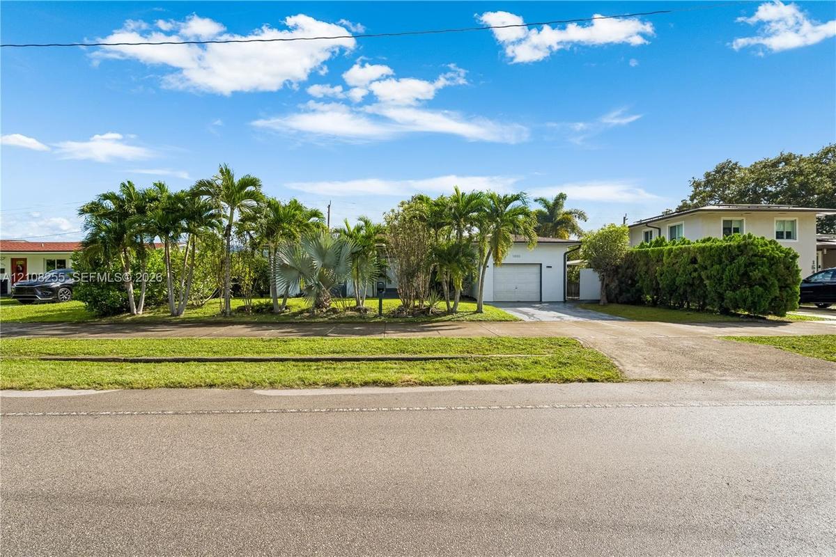 Exterior of a single-story residence featuring a concrete driveway, attached garage, manicured lawn, and mature palm landscaping