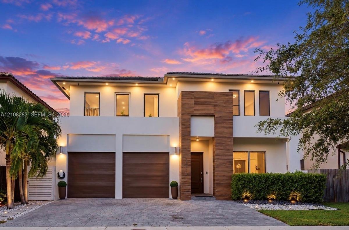 Two-story contemporary exterior featuring stucco siding, vertical wood-finish accents, dual-car garage, recessed exterior lighting, and a paved stone 