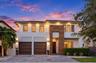 Two-story contemporary exterior featuring stucco siding, vertical wood-finish accents, dual-car garage, recessed exterior lighting, and a paved stone 