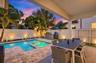 Covered patio featuring stone-paver decking, integrated swimming pool with inset spa, built-in stainless steel outdoor kitchen, and perimeter privacy 