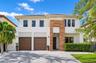 Two-story exterior featuring smooth stucco finish, vertical wood-plank architectural cladding, paver driveway, and dual wood-finish garage doors