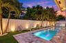 Backyard featuring a rectangular swimming pool, stone-paver decking, integrated outdoor kitchen, artificial turf, and perimeter wall lighting