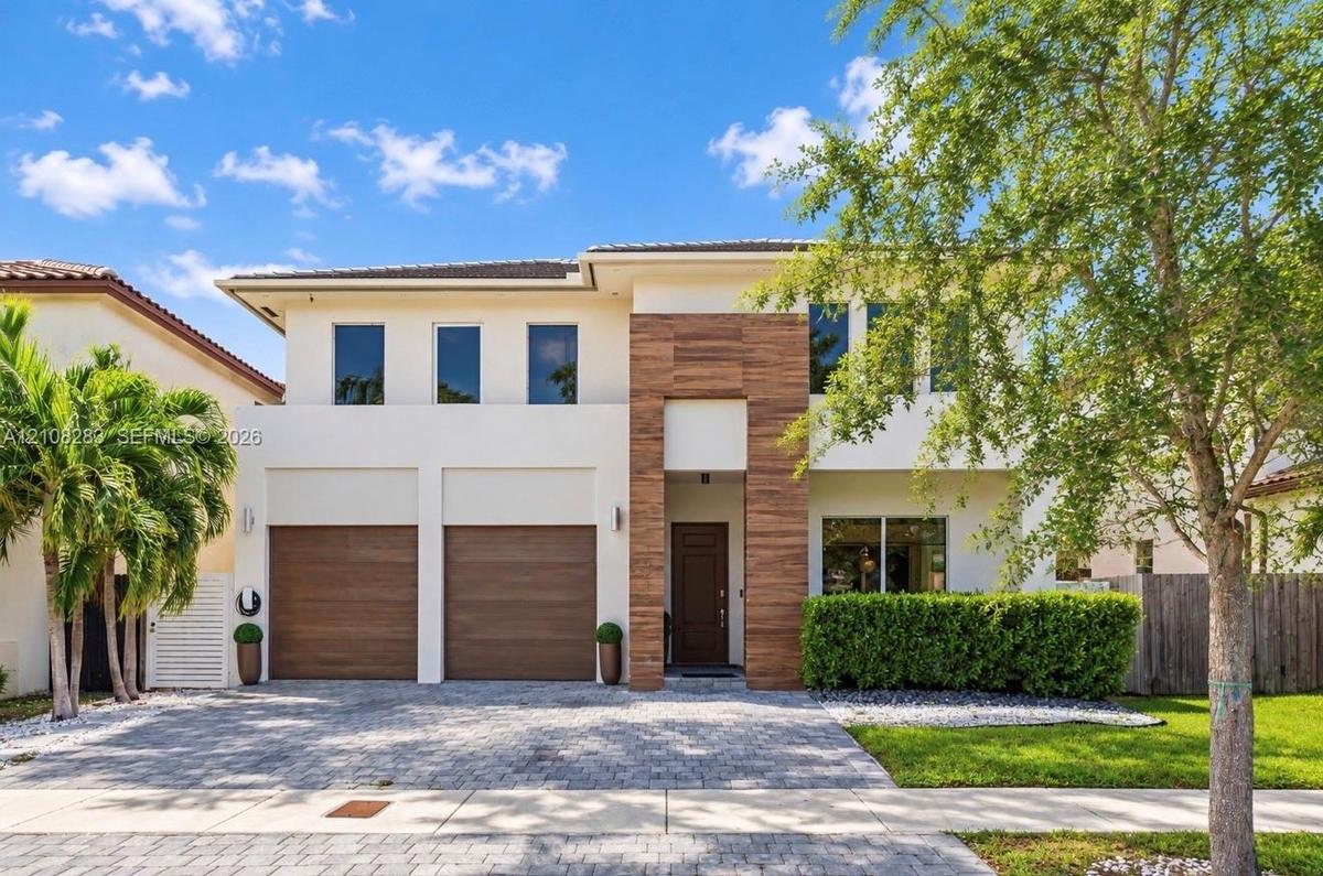 Two-story exterior featuring light-toned stucco, wood-finish accents, a paver driveway, and an attached two-car garage