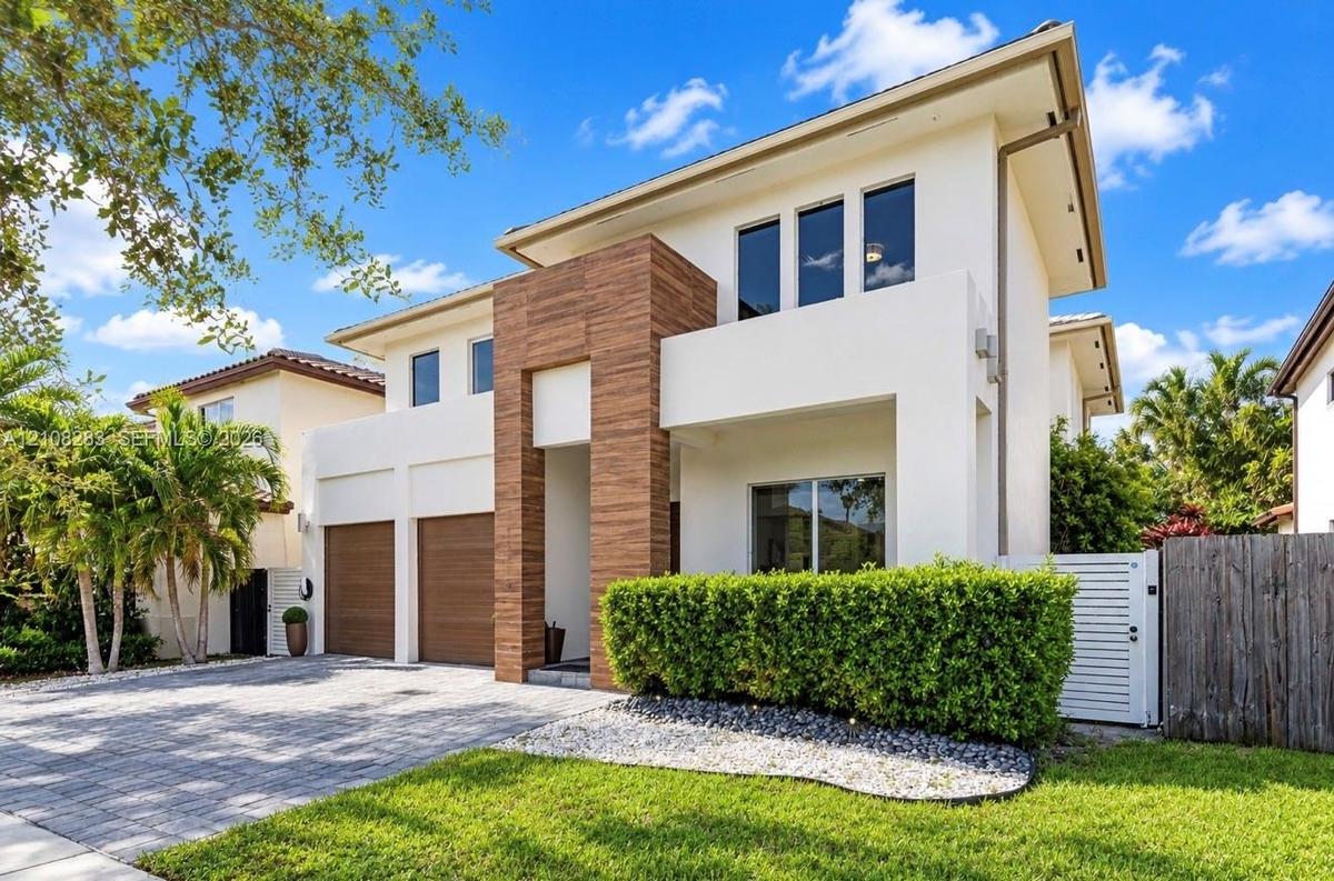 Modern two-story exterior featuring a smooth stucco finish, wood-tone architectural detailing, a paver driveway, and a double-car garage