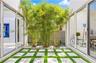 Interior courtyard featuring floor-to-ceiling glass sliding doors, concrete paver grid, synthetic turf, mature bamboo, and perimeter privacy fencing