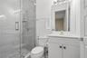 Glass-enclosed shower with stone-tile flooring, wall-mounted handheld shower head, vanity with integrated basin, and modern light fixture