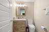 Bathroom featuring a wood-finish vanity with a rectangular sink, wall-mounted light fixture, framed mirror, and elongated dual-flush toilet