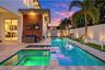 Outdoor living area featuring a rectangular swimming pool with an integrated spa, stone paver decking, horizontal wood-slat accent wall, and perimeter
