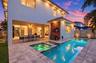 Rear exterior featuring a covered patio, rectangular swimming pool with integrated spa, stone paver decking, and horizontal wood-slat wall cladding