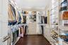 Walk-in closet featuring floor-to-ceiling custom built-in shelving, glass display shelving with integrated lighting, multi-tiered hanging rods, and in