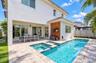 Backyard featuring an in-ground swimming pool, integrated spa, stone paver decking, white exterior siding, and vertical wood-slat accent wall