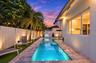 Rectangular swimming pool featuring a stone-paver surround, integrated spa, built-in outdoor grill station, and artificial turf lawn, enclosed by priv