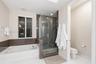 Built-in soaking tub with a tiled surround, glass-enclosed shower, polished finish flooring, and wall-mounted metal fixtures
