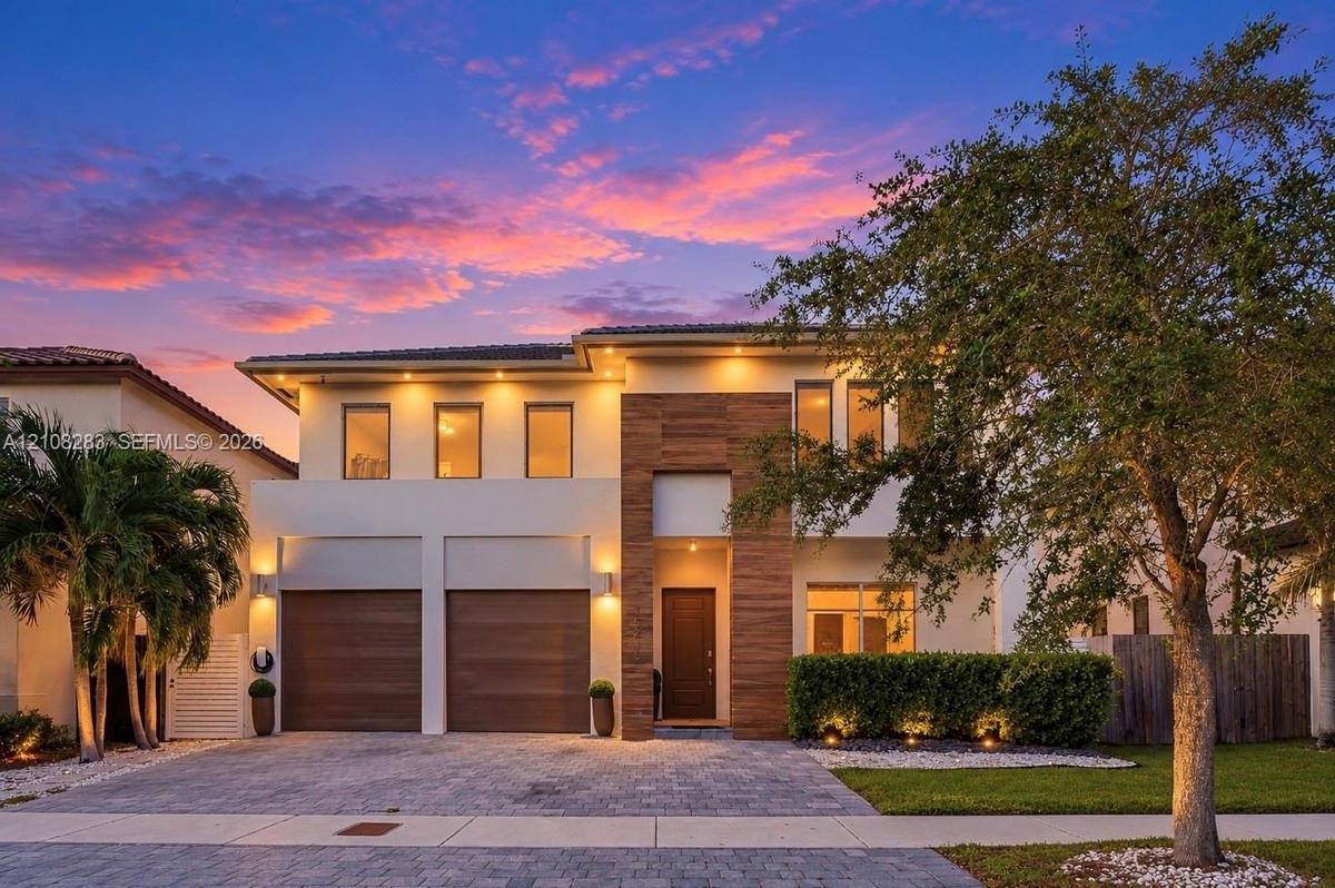 Two-story contemporary exterior featuring a light-toned stucco facade, wood-finish accents, integrated soffit lighting, a two-car garage, and a paver 